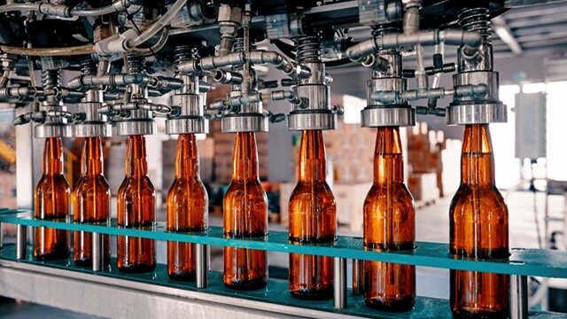 Row of amber glass beer bottles being filled on an automated production line in a brewery